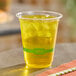 A clear 12 oz. compostable plastic cold cup filled with a yellow beverage and ice.