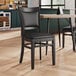 A black Lancaster Table & Seating chair with a wooden frame and black vinyl seat sits at a table in a restaurant.