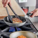 A person using a Vollrath Wear-Ever non-stick fry pan to cook meat on a stove.