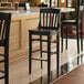 A Lancaster Table & Seating black wood school house bar stool next to a counter.
