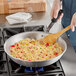 A person cooking rice in a Vollrath Wear-Ever aluminum fry pan.