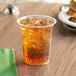 A World Centric plastic cup filled with a drink on a table with a sandwich.