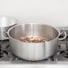 A Vollrath Optio brazier pot on a stove with food inside.