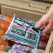 A hand holding a Lifoam Freez Pak reusable ice pack bag in a cooler with frozen food inside.