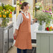 A woman in an Acopa Cinnamon Linen Smock Bib Apron holding a bouquet of flowers.