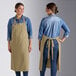 Two women wearing Acopa Ashville sage linen bib aprons on a counter in a professional kitchen.