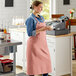 A woman wearing an Acopa Ashville mauve linen bib apron holding a cup of coffee.