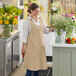 A woman wearing a tan Acopa Ashville smock bib apron with 2 pockets.