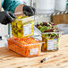 A person in gloves uses a pen to label a Carlisle clear plastic food pan on a counter.