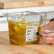 A person using a marker to write on a Carlisle clear plastic food pan filled with yellow liquid.