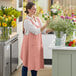 A woman in an Acopa Ashville mauve linen smock bib apron arranging flowers in a vase.