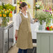 A woman wearing a sage linen smock bib apron with 2 pockets.