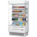 A Turbo Air white narrow vertical air curtain display case filled with bottles of drinks.