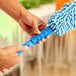 A person using a Lavex Flex Wand Duster with a blue microfiber sleeve on the end.