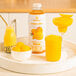 A tray with a glass of yellow Smartfruit Mellow Mango beverage next to a jar of yellow Smartfruit Mellow Mango puree.