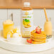 A bottle of Smartfruit Sunny Banana Puree on a table with a bowl of ice cream, strawberries, and yellow pancakes.