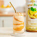A glass of Smartfruit banana smoothie with a straw next to a container of Smartfruit Sunny Banana puree.