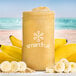 A jar of Smartfruit Sunny Banana puree next to bananas and oats with a yellow smoothie inside.