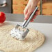 A hand using a Choice stainless steel dough docker with metal pins to dock pizza dough.