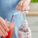 A hand using a Smartfruit Puree Pump to pour red liquid into a glass.