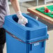 A woman in gloves putting a plastic bag in a dark blue Lavex slim rectangular trash can.