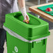 A gloved hand puts food into a lime green Lavex compost receptacle.