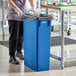 A woman in a blue uniform putting a black garbage bag in a Lavex dark blue rectangular trash can.