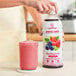 A woman pours Smartfruit Blooming Berry puree into a glass.