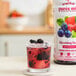 A bottle of Smartfruit Blooming Berry puree next to a glass of berry drink with berries inside.