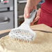 A person using a Choice 5" wide dough docker with white plastic pins to roll white pizza dough.