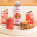 A white container of Smartfruit Superfruit All-Stars Puree on a table with a glass of pink drink and a bowl of fruit.