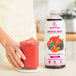 A woman holding a glass of red Smartfruit Superfruit All-Stars puree next to a bottle of the mix.