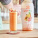 A plastic bottle of Smartfruit Tropical Harmony Puree next to a glass of fruity drink.