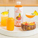 A glass jar of Smartfruit Tropical Harmony puree with a drink in it and a slice of orange on the rim.