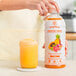 A hand holding a bottle of Smartfruit Tropical Harmony puree next to a glass of yellow liquid.