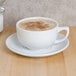 A white CAC Clinton cappuccino cup on a saucer with brown foam in it.