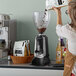 A woman in a brown apron pouring coffee beans into a HeyCafe espresso grinder.