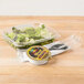 A Genpak clear plastic deli container with salad and lettuce, and a fork on a table.