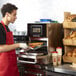 A man in a red apron putting food into a Merrychef conneX12 high-speed oven.