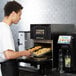 A man in a white shirt putting food into a Merrychef conneX12 high-speed oven tray.