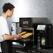 A man standing in a professional kitchen putting food into a Merrychef conneX12 high-speed oven.