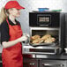 A woman in a red apron using a Merrychef conneX16 high-speed oven to cook sandwiches.