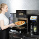 A woman cooking a pizza in a Merrychef conneX12 high-speed oven.