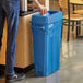 A man standing next to a Lavex Pro blue slim rectangular trash can with white text.