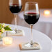 Two Schott Zwiesel burgundy wine glasses filled with red wine on a table with candles.