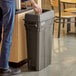 A man putting a Lavex Pro gray rectangular trash can into a trash can.