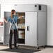 A woman opening a Delfield reach-in refrigerator in a school kitchen.