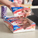 A hand holding a box of Hostess Glazed Strawberry Jumbo Donuts over a counter with a cash register.