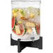 A clear acrylic beverage dispenser with white liquid and fruit inside.