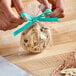 A hand tying a blue ribbon to a LK Packaging candy bag holding a cookie.